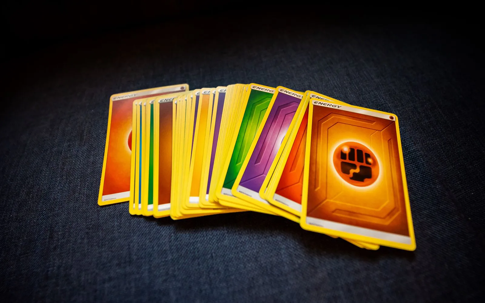 Cartes Énergie Pokémon dorées étalées en éventail sur un tissu sombre