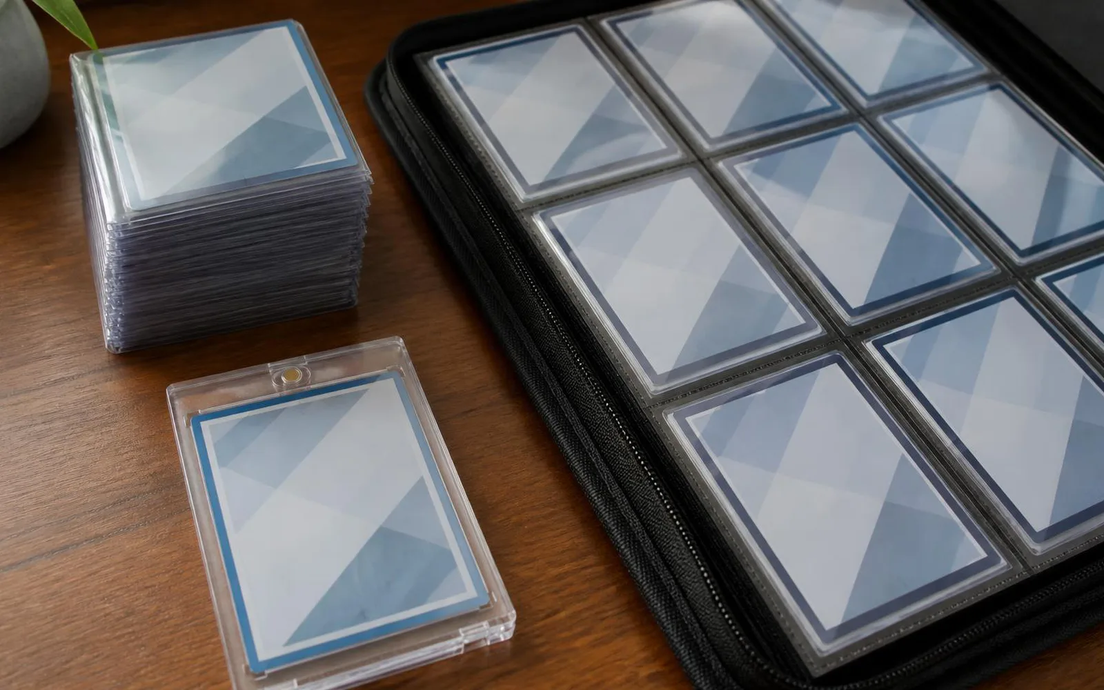 Cartes sous protections rigides empilées à côté d'un classeur zippé ouvert, sur un bureau en bois